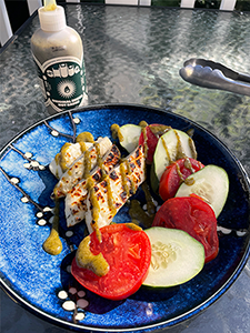 Grilled Halloumi with tomato and cucumber slices and a bottle of Shuug Zhoug Hot Sauce